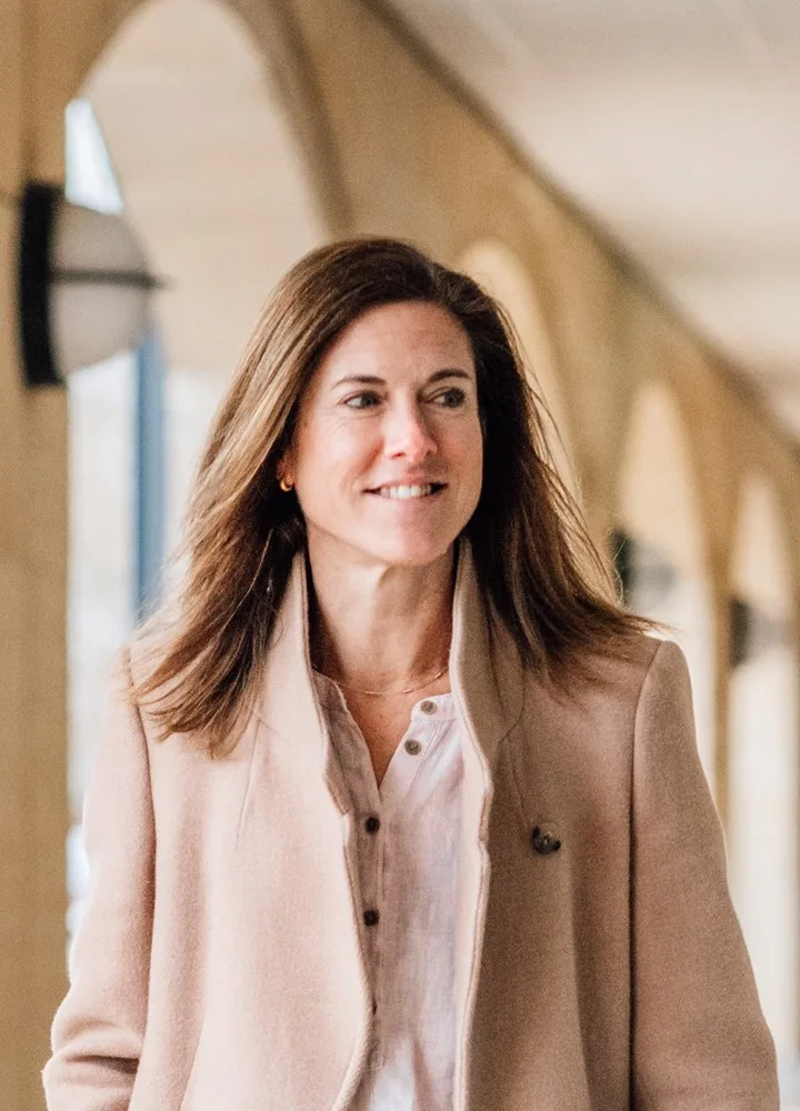 Lisa LLoyd walking beneath a stone colonnade, smiling